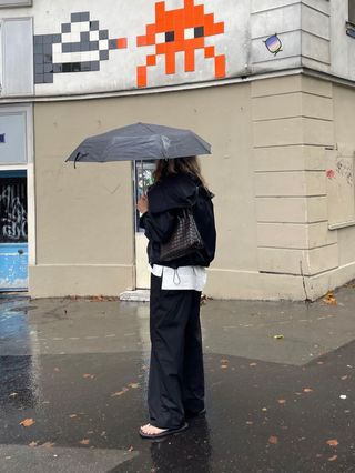 Eliza Huber wearing a black sporty Proenza Schouler jacket with a white poplin shirt, black poplin pants, and flip flops in Paris.