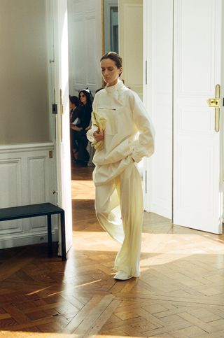 An SS24 runway photo at The Row that shows a cream nylon sporty anorak jacket with cream trousers and white flats.