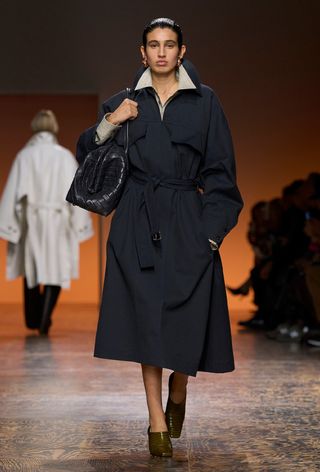 the navy color trend shown on Bottega Veneta's fall runway worn by a model wearing gold earrings, a white button-down, a navy trench coat, brown mules, and a navy handbag