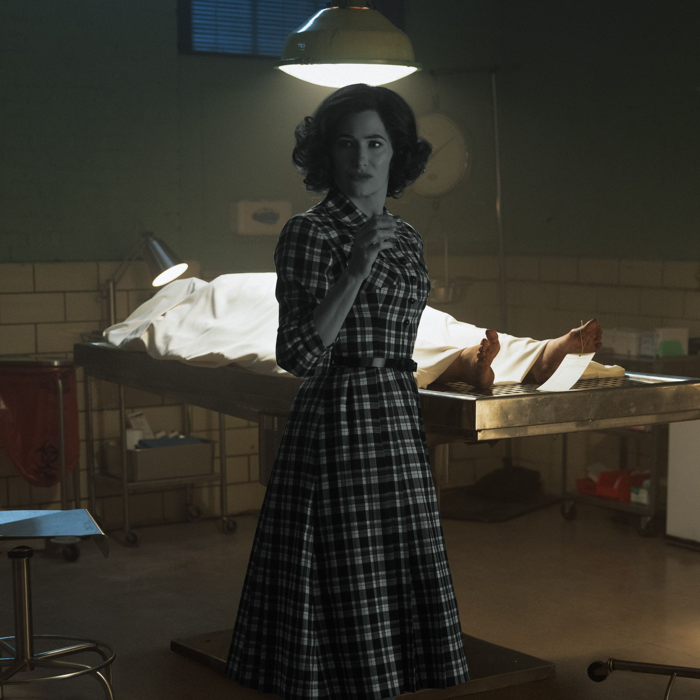 A woman drained of all color saturation standing in a fully colorized morgue.