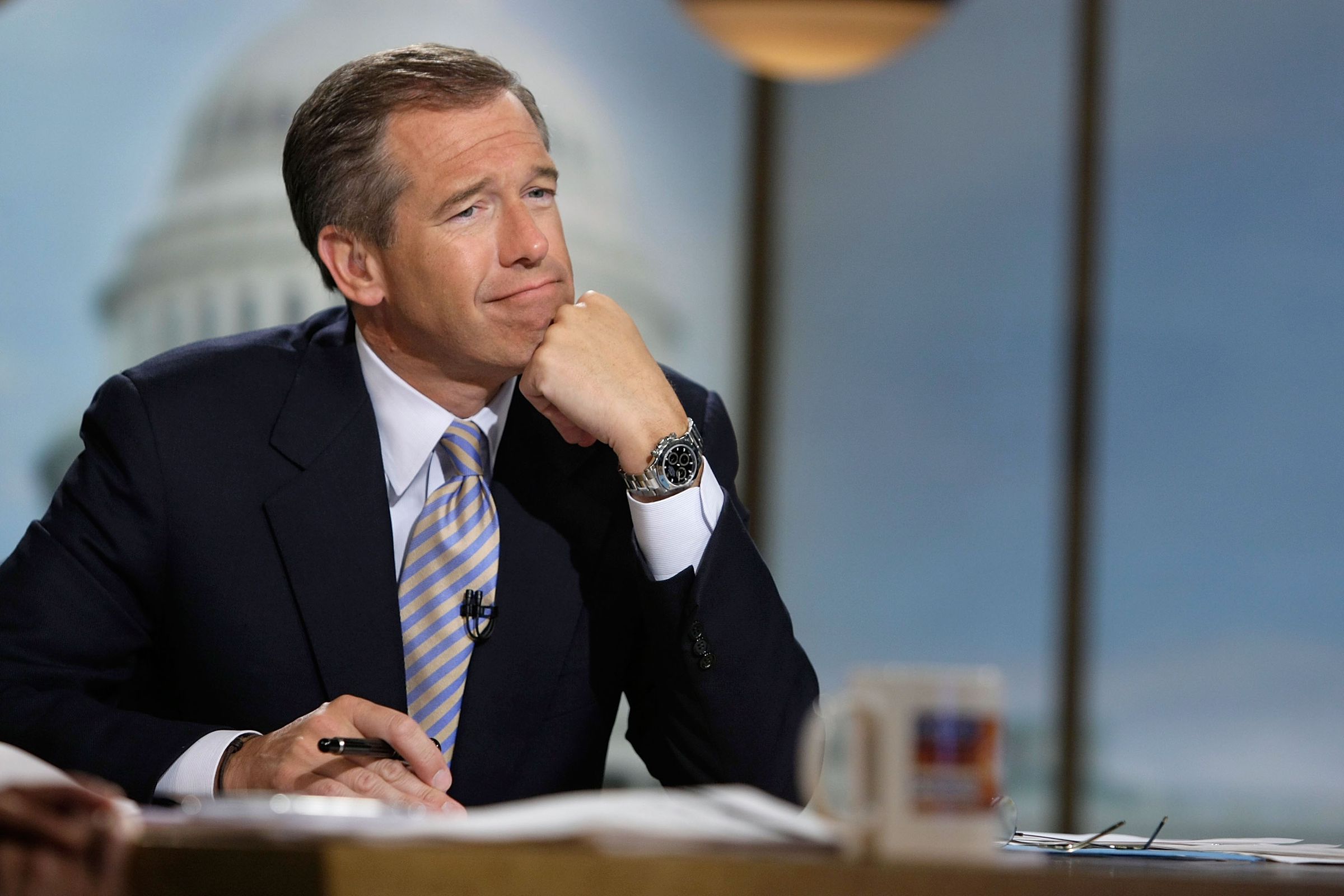 Brian Williams sitting at a desk, with his chin resting on his fist.