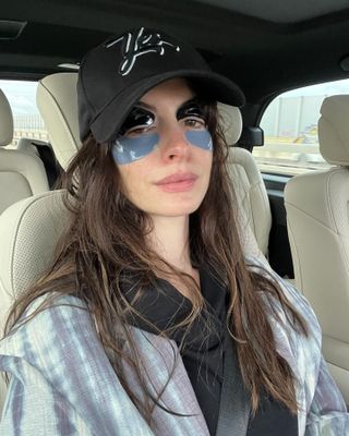 Anne Hathaway wearing a baseball cap with two sets of under eye masks on.