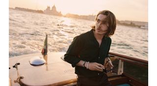 Wolfs actor Austin Abrams arrives at the 2024 Venice Film Festival by boat wearing a black button-down shirt.