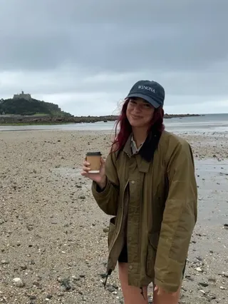 Dua Lipa wears a waxed jacket on the beach with shorts and a baseball cap