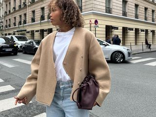 Ellie Delphine in a double-breasted jacket, T-shirt, jeans, and a burgundy clutch.