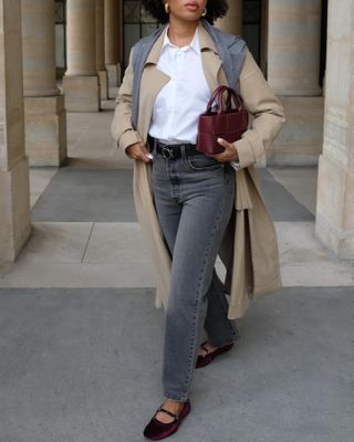 French woman wearing a trench coat, jeans, and ballet flats.