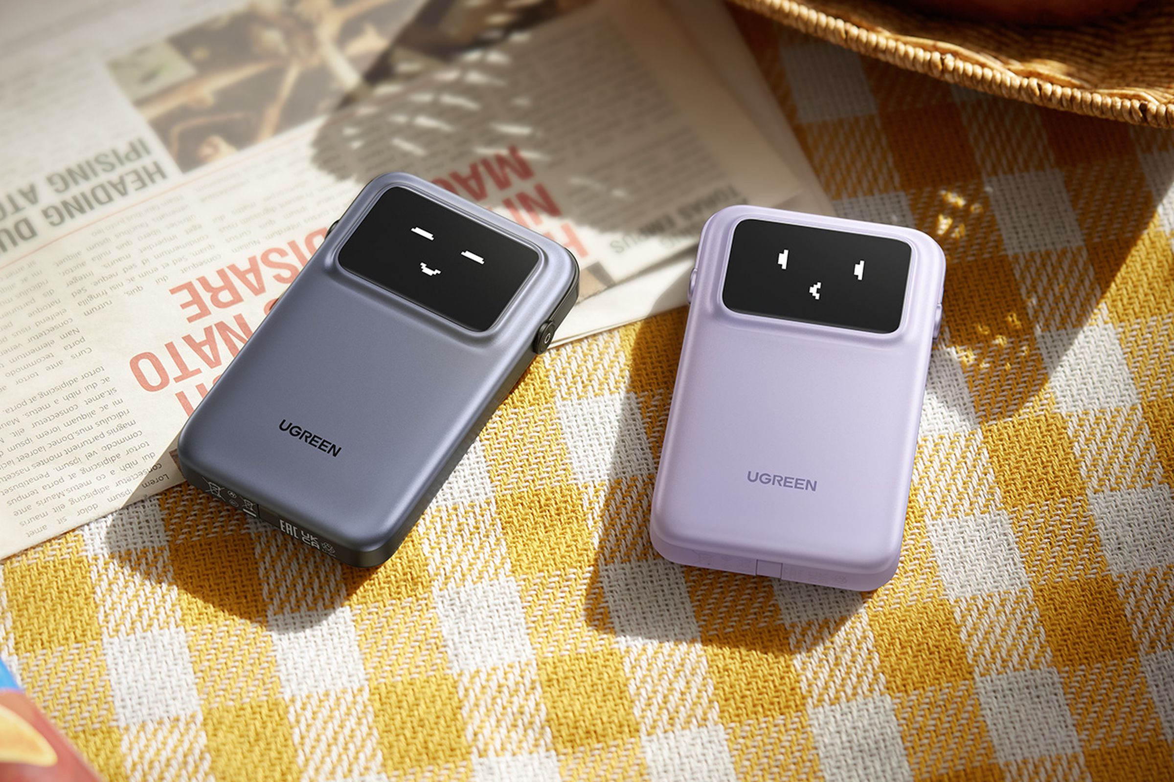 A pair of Ugreen Uno power banks sitting on a table, showing their emoji face status screens.