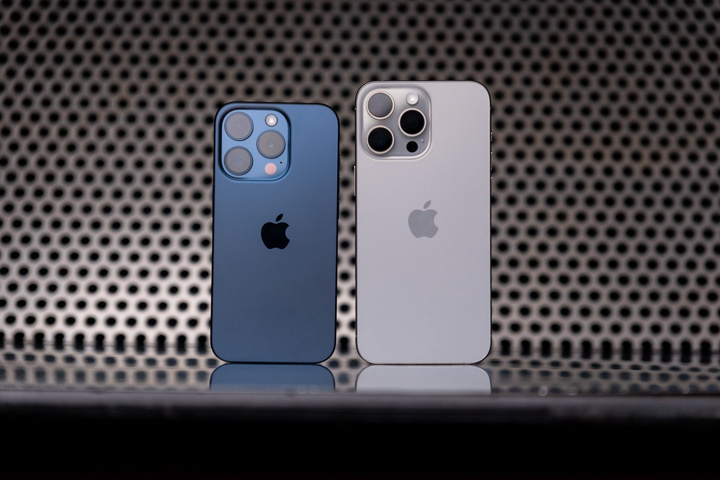 The iPhone 15 Pro (blue titanium) and 15 Pro Max (white titanium) standing next to one another.