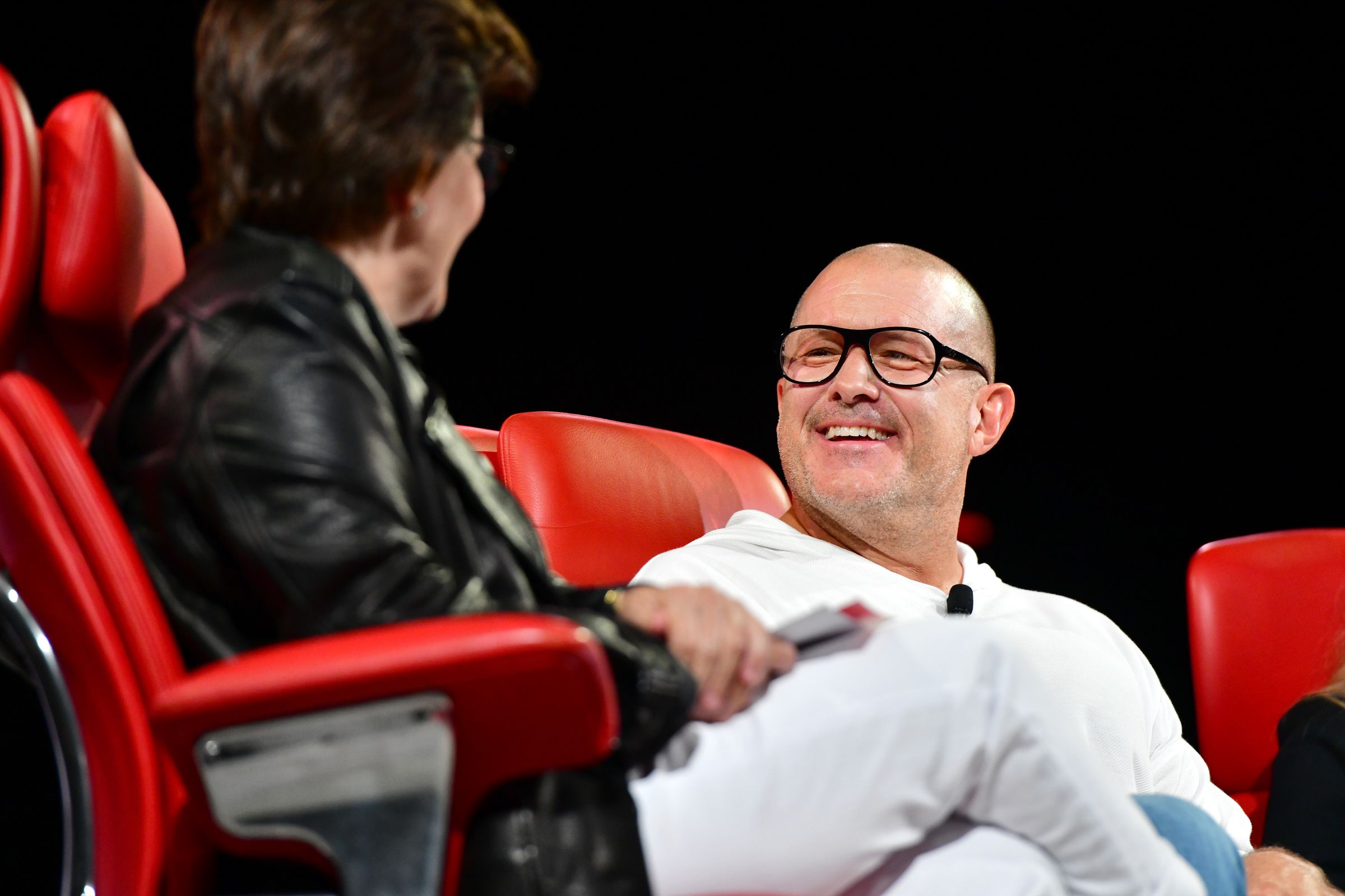 An image of a smiling Jony Ive sitting in a bright red chair. 