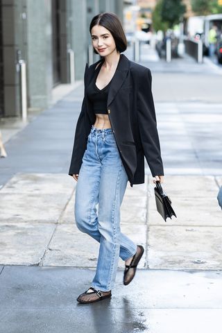 Lily Collins wearing a black blazer, jeans, and Alaia ballerinas