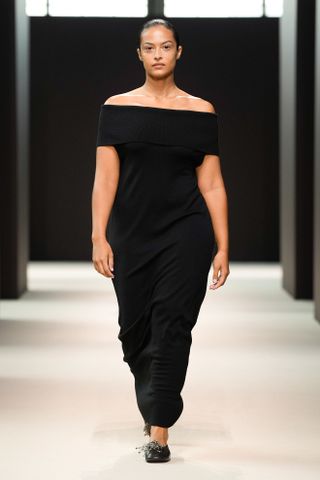 A woman wears an off-the-shoulder black maxi dress with black ballet flats.