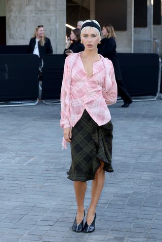 Iris wears a pink checkered print top, a green midi skirt, black heels, and a black headband.