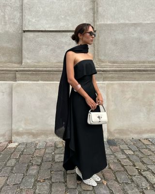 Debora Rosa wearing a black strapless dress with a matching scarf, white bag, and white heels.