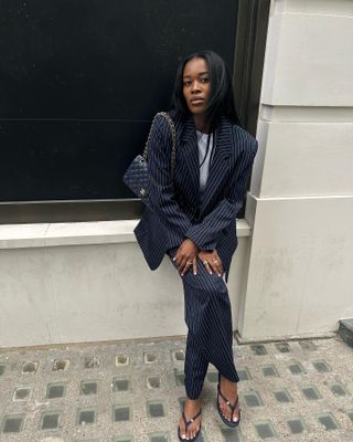 @nlmarilyn wearing a navy blue pinstripe suit with a navy blue Chanel quilted flap bag and black flip flops.