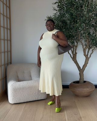 Abi wears an ivory knit maxi dress, a gray shoulder bag, and green mules.