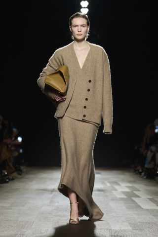 Woman in beige cardigan and knit skirt on Ferragamo runway.