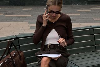 Woman in brown cardigan and shorts on the phone.