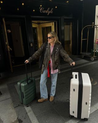 Lucy wears a brown leather jacket, red striped button down, blue jeans, brown boat shoes, and sunglasses.