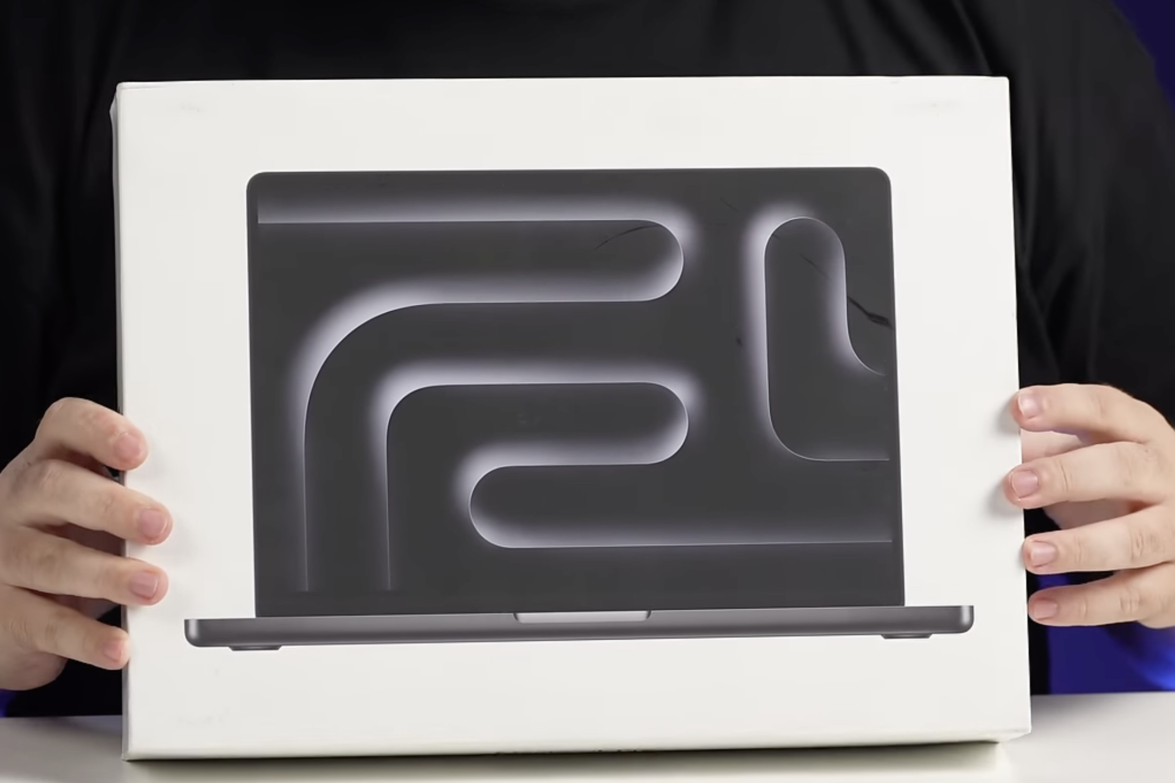 A MacBook Pro box being held between two hands so that the top label is facing the camera.