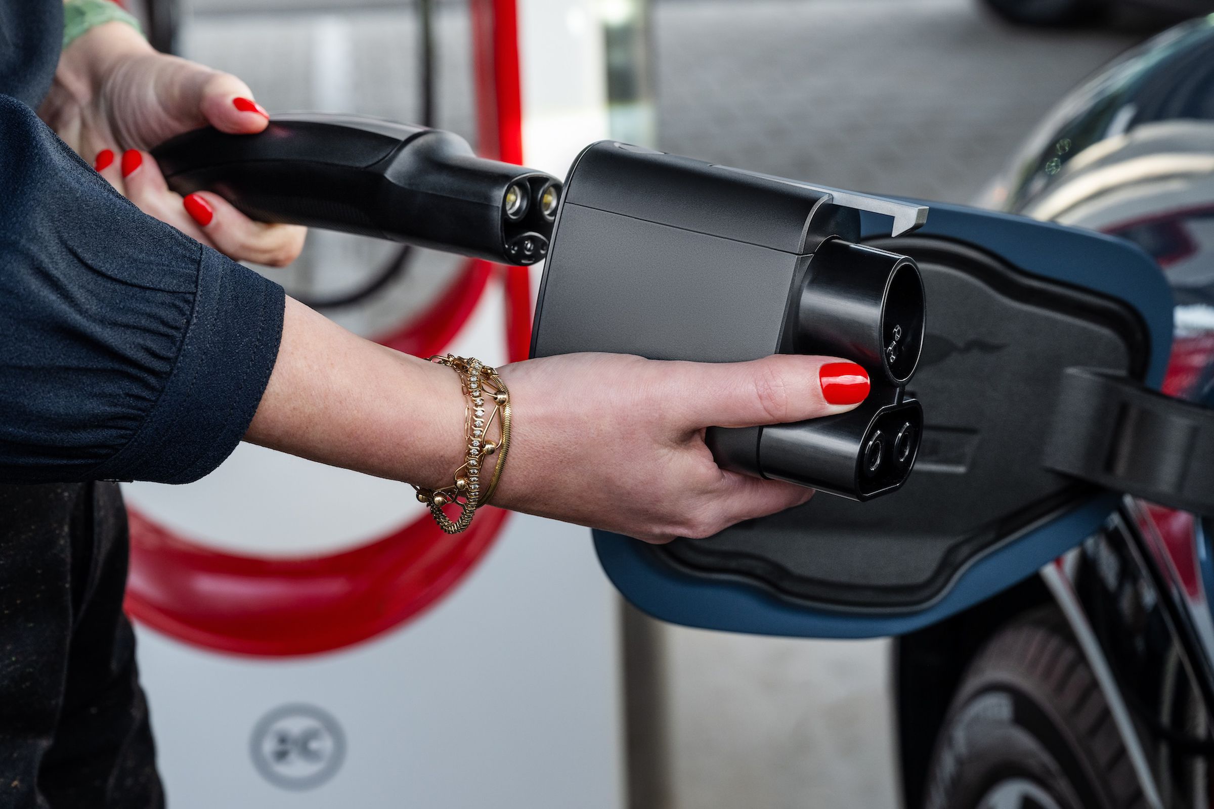 A person plugging a Tesla Supercharger plug into a Ford vehicle via the Ford NACS adapter.