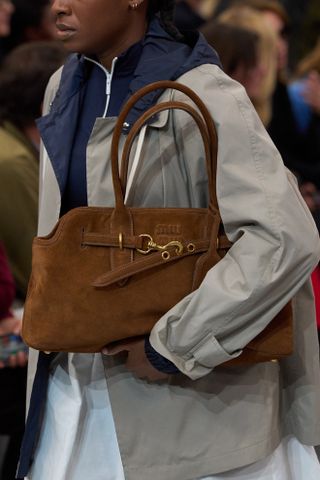 A close-up image of a brown suede top-handle east-west bag at the Miu Miu spring summer 2025 runway show in Paris.