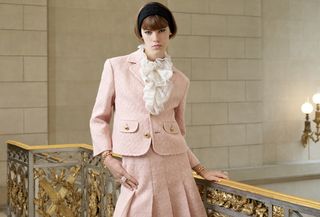 A woman wearing a black headband, pink blazer, ruffle blouse, and pink skirt for Celine's spring/summer 2025 collection.