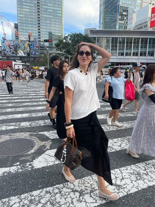 Anna LaPlaca wearing a white Naadam T-shirt with a black midi skirt and white mesh flats in Tokyo