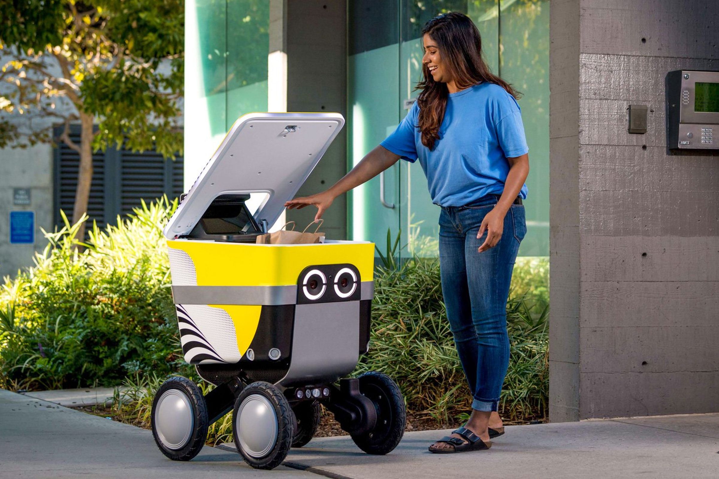 A person removes a bag of food from a Serve delivery robot with its lid open.