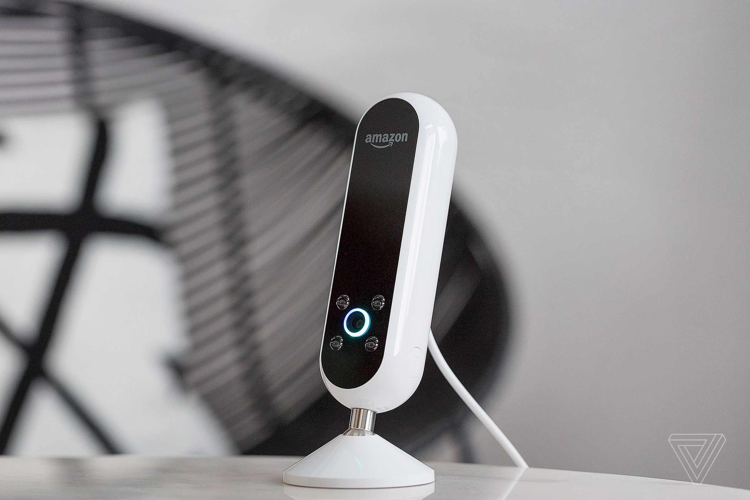 The Amazon Echo Look camera perched on its stand on a table with a cord dangling behind it.