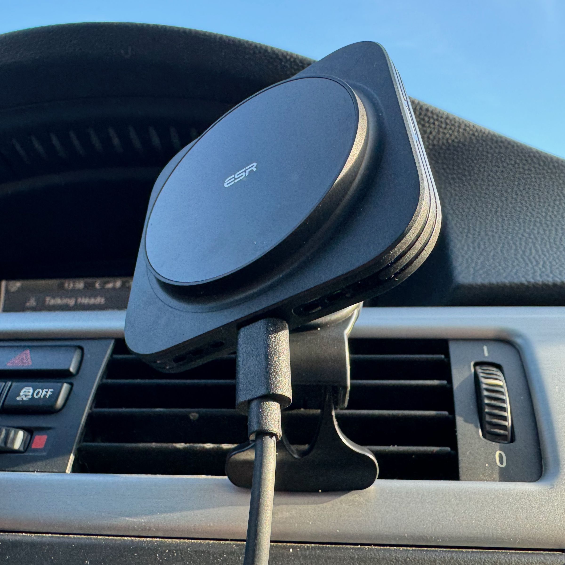 A black plastic car charging mount with the ESR logo at the center of the circular charging puck is mounted to a car’s vent.