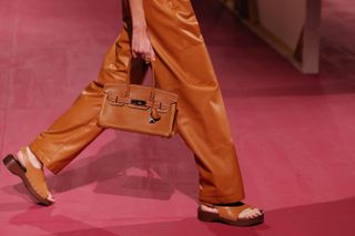 a detail image of an Hermes model walking the spring/summer 2025 runway wearing leather pants and clog sandals