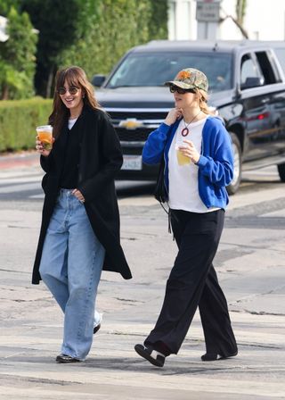 Dakota Johnson wore round sunglasses, a black sweater, white t-shirt, black coat; Jennifer Lawrence wears a camo hat, oversize sunglasses, a white t-shirt, pendant necklace, blue zip-up sweatshirt, and black sweatpants.