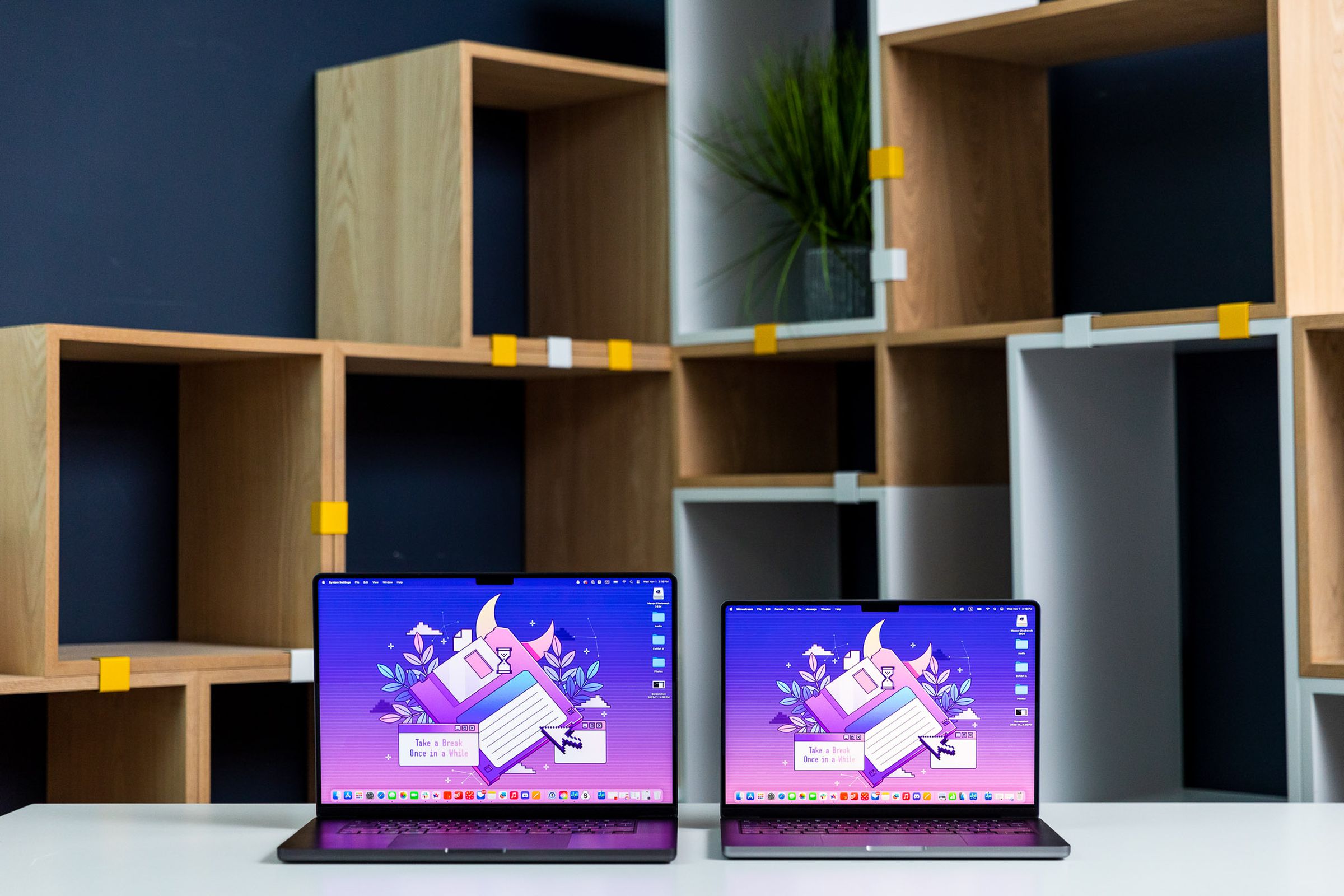 M3 Max MacBook Pro 16 next to an M3 MacBook Pro 14 in front of boxy geometric bookshelves