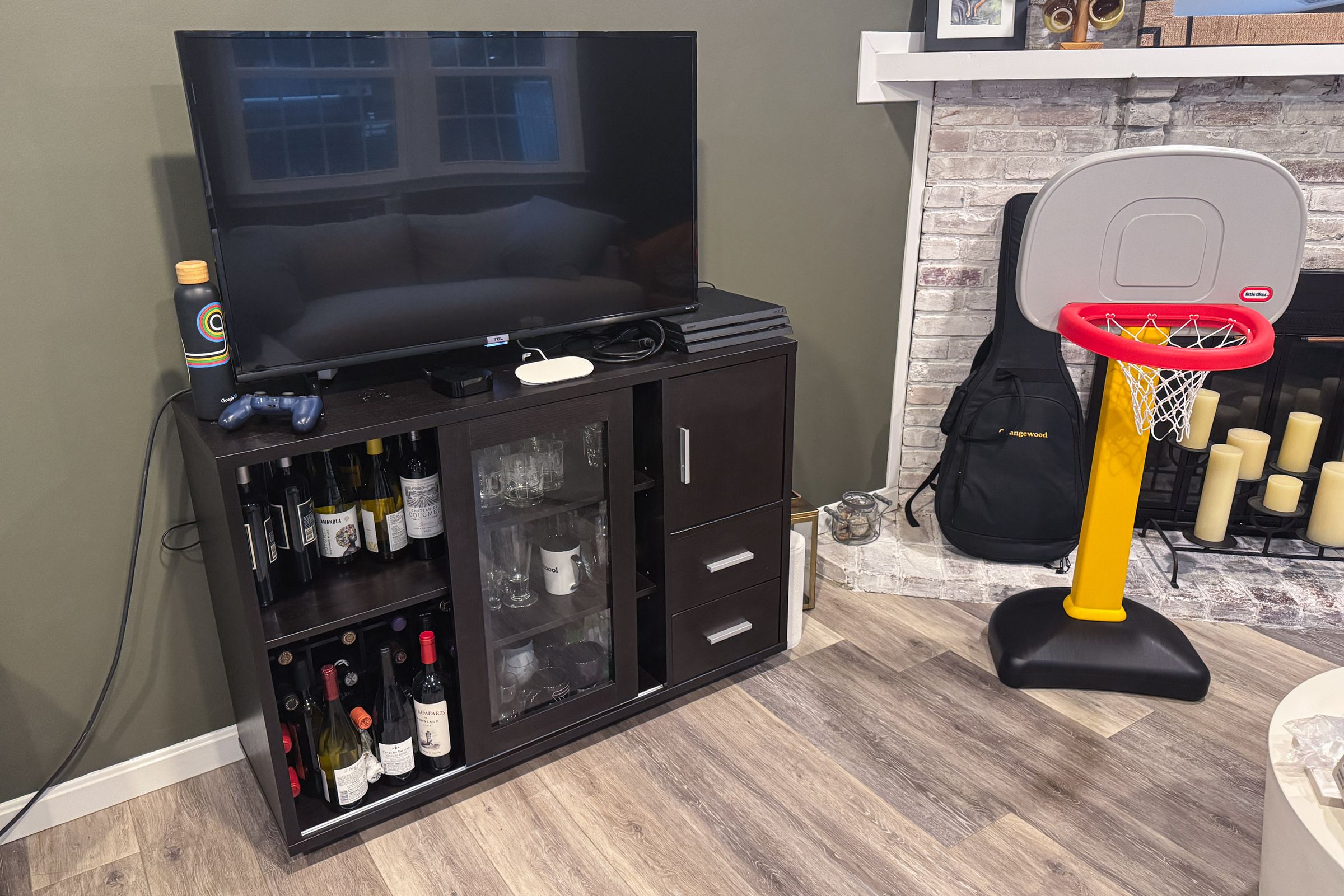 TV on top of liquor cabinet with toy basketball net and fireplace.