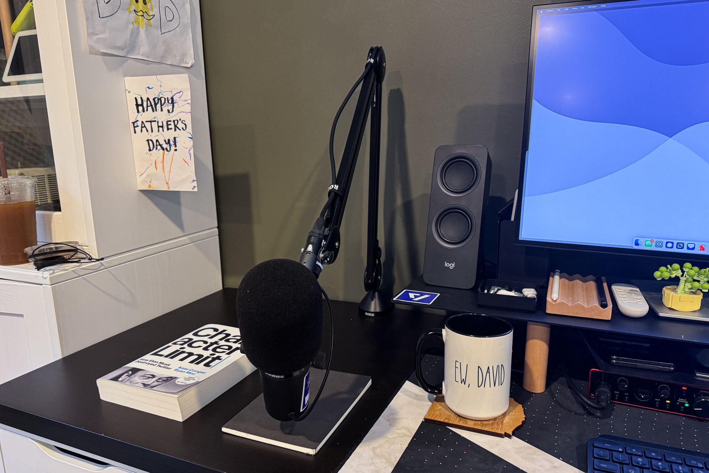 Desk with book and mic next to a bookcase that had a kid’s father’s day card taped to it.