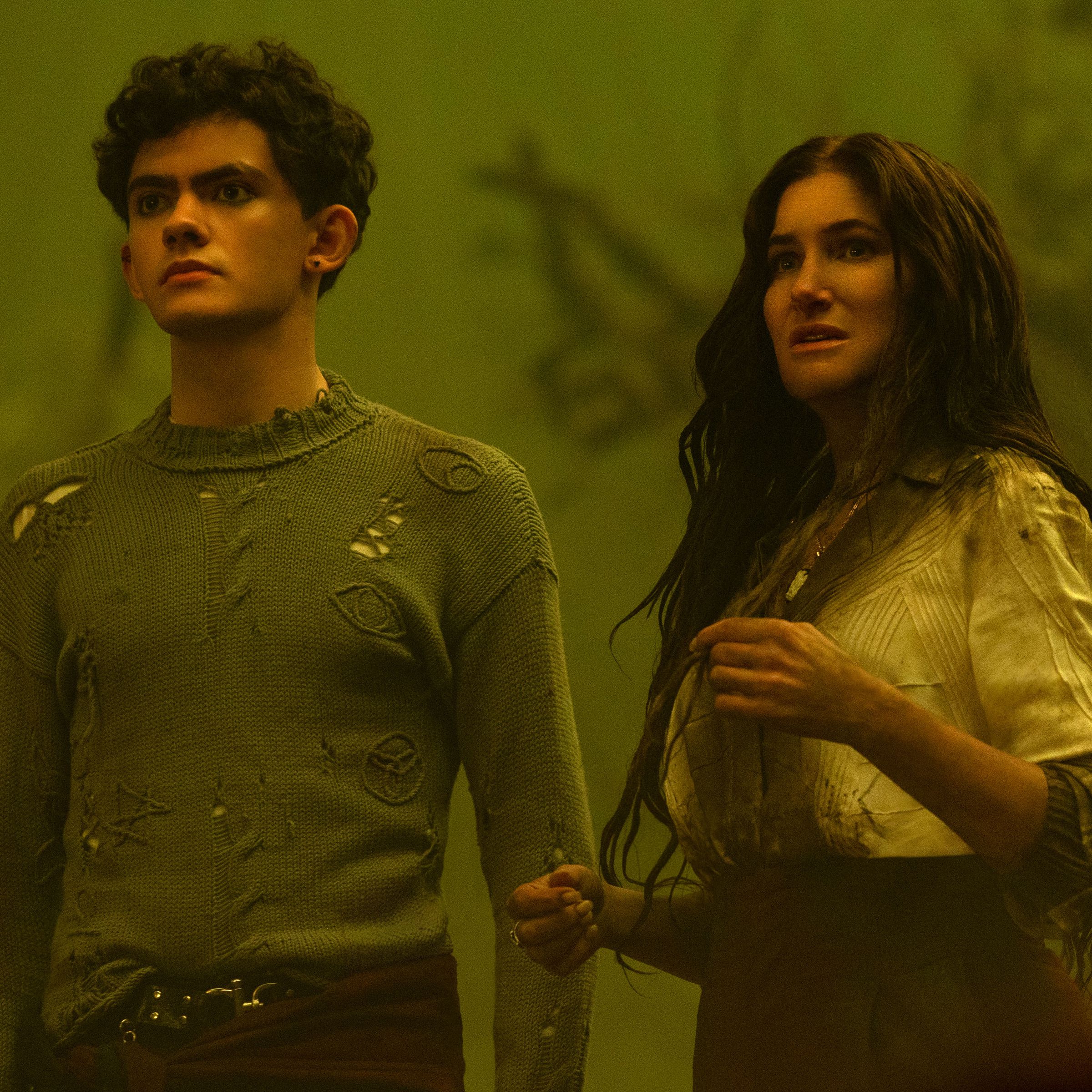 A teenage boy and a woman standing together in what appears to be a foggy woods bathed in yellow-green light.