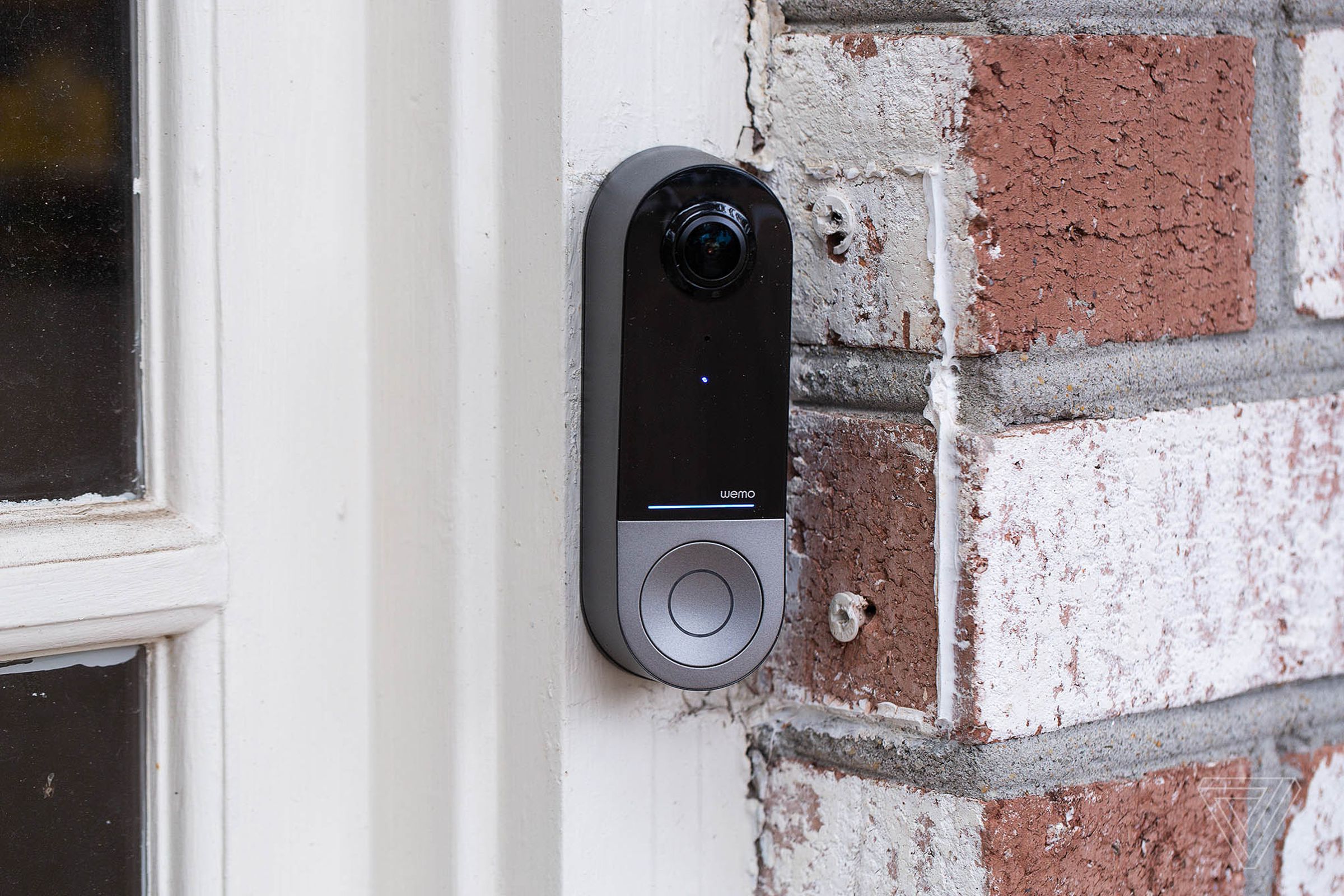 A black and silver doorbell with a camera on a brick wall.