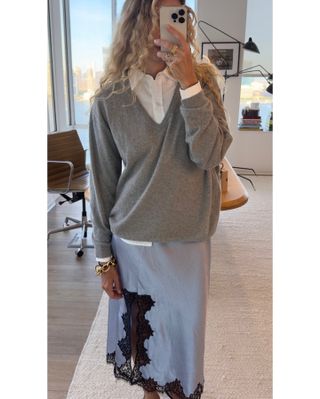 Olympia wears a white button-down shirt, gray v-neck sweater, and silver lace-trim slip skirt.