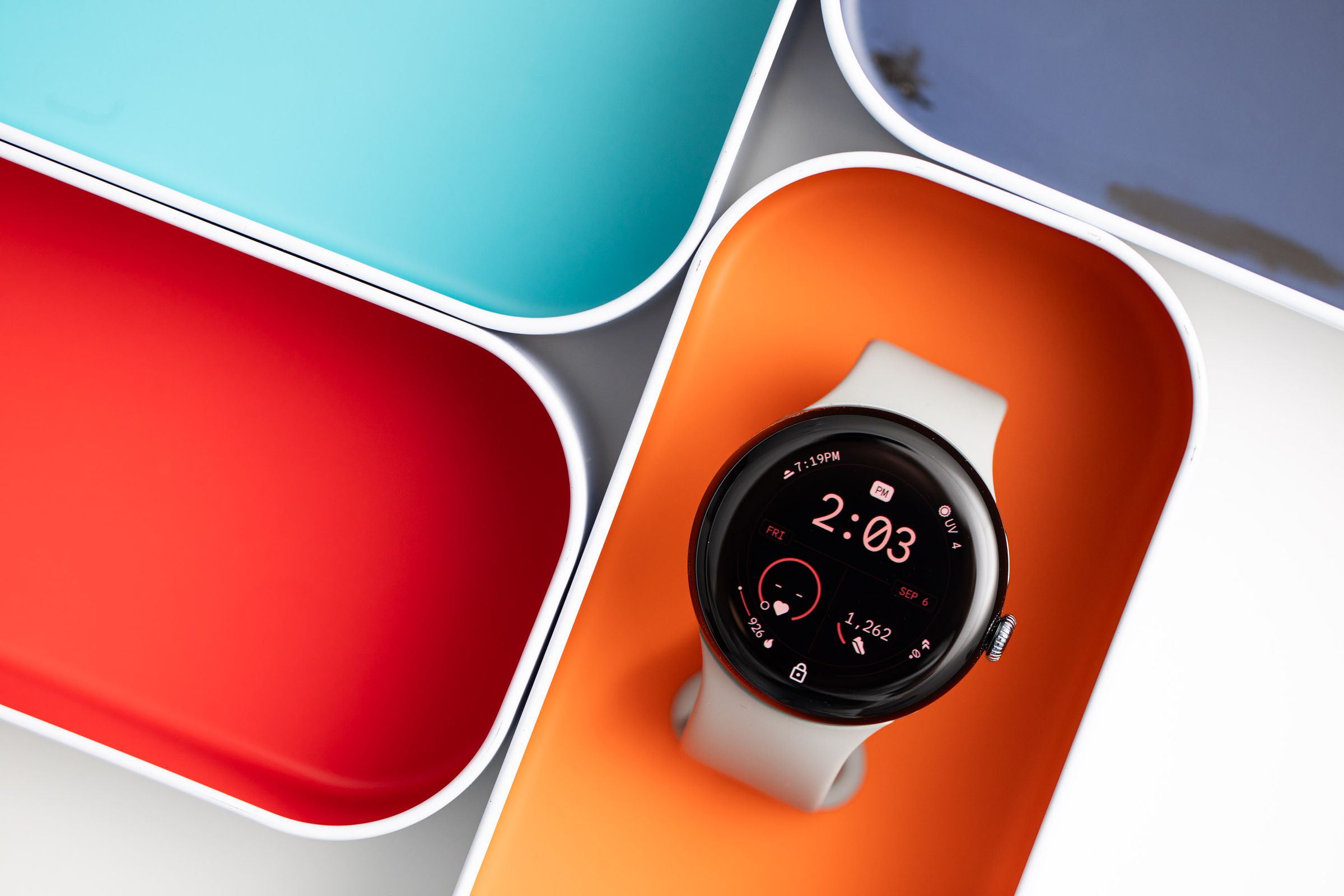 The Google Pixel Watch 3 resting in an orange case box surrounded by other colorful boxes.