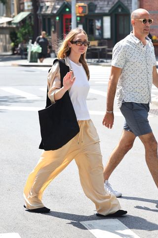 Jennifer Lawrence wearing a white T-shirt, yellow button-down shirt, yellow silk pants, a black tote bag, and black slippers while walking across the street in New York City.