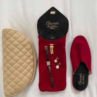 A flat lay showing Cartier jewelry and red Charvet slippers.