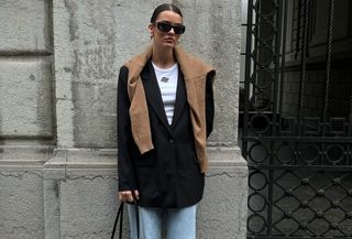 Mary wears a white t-shirt, black blazer, brown sweater, blue jeans, black boots, and a large black east-west bag.