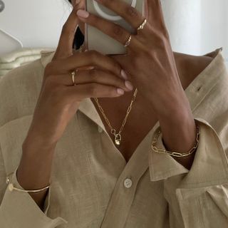 Woman wearing simple gold jewelry, including paperclip bracelets and rings.