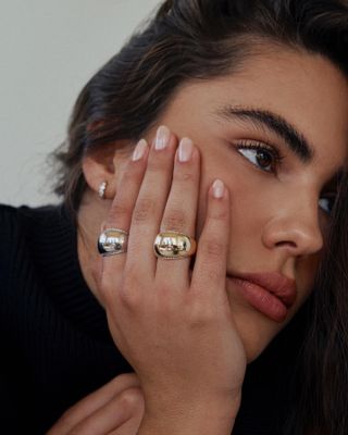 Woman holding head in hand, wearing gold and silver chunky rings.