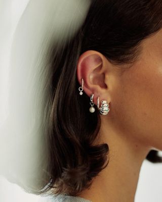 Woman wearing silver earrings and silver hoops with pearls.