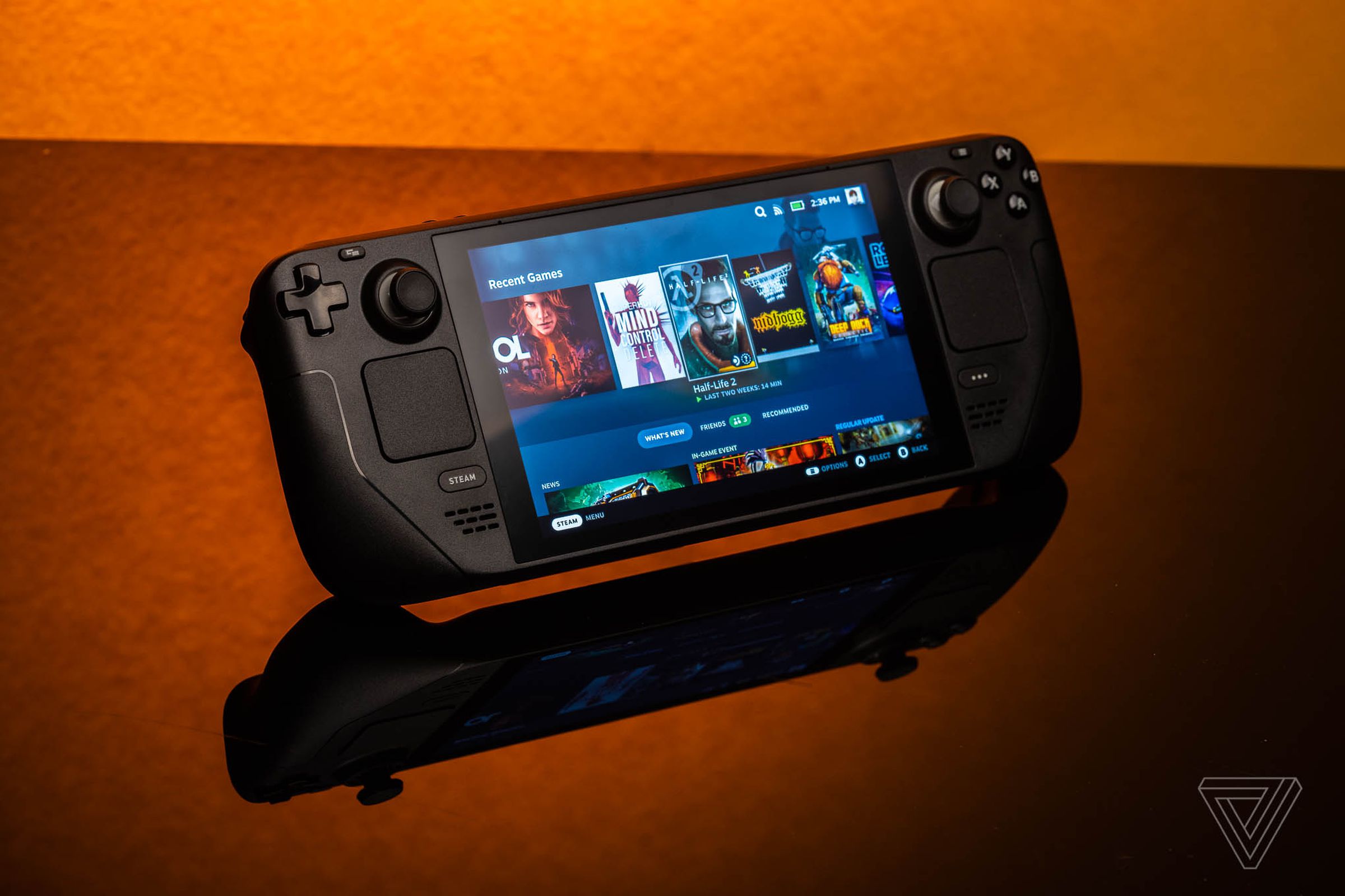 The Valve Steam Deck gaming handheld sits on a reflective table, with an orange background.