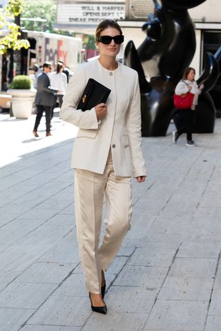 A woman wears a cream blazer with a pair of cream satin trousers