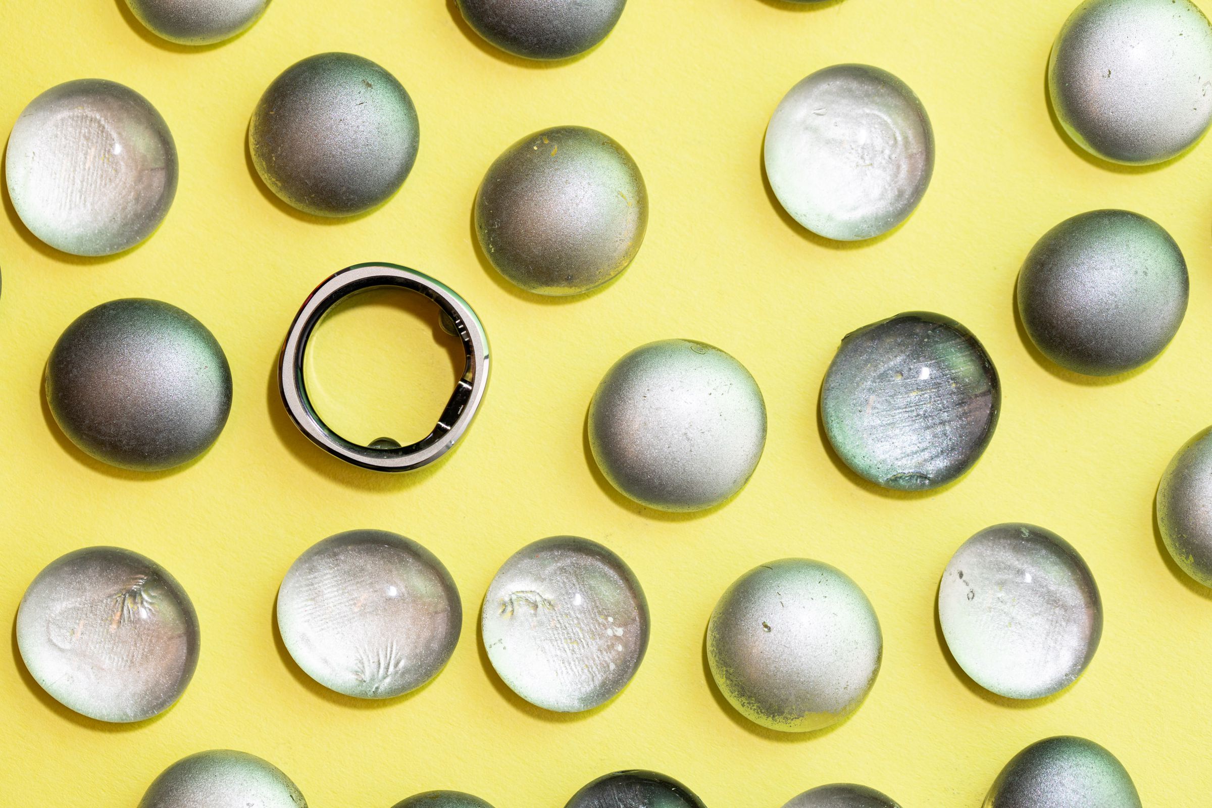 A smart ring shot from amid a group of stones and glass globes on a yellow background.