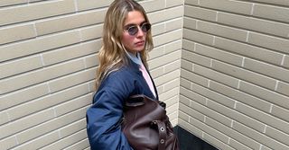 Torivan wears blue bomber and brown athletic pants with a pink stripe while holding a large brown leather tote