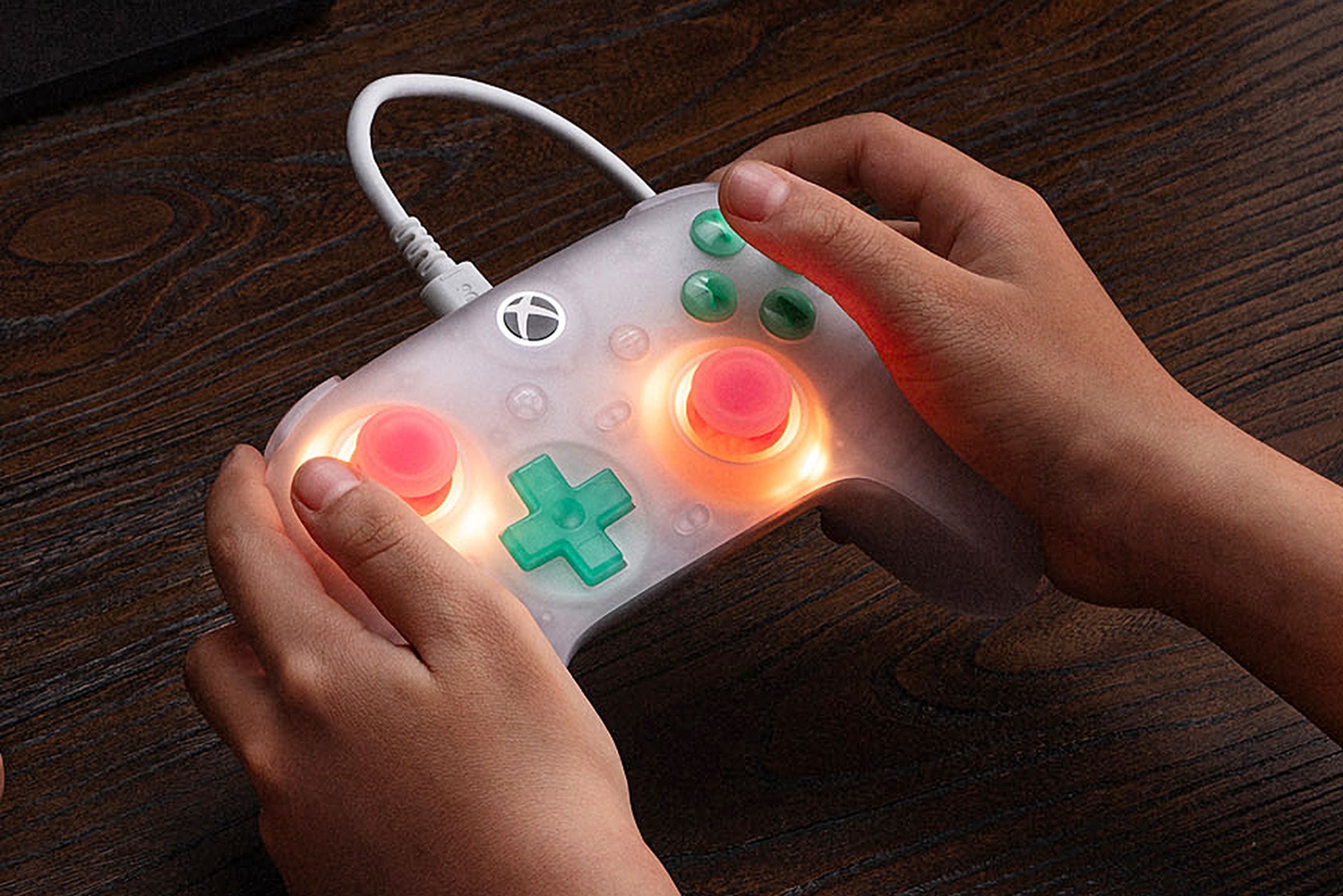 The 8BitDo Ultimate Mini controller being held in two hands with its joysticks glowing.